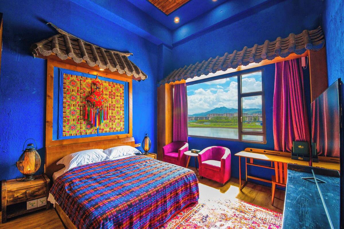 A room with a bed, a desk, a chair, and a window with a view of a landscape.