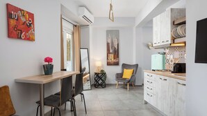 A modern kitchen with white cabinets, a dining area with a wooden table and chairs, and a cityscape painting on the wall. - Acropolis Sandra Deluxe Apartment, Bill & John Apartments & Villas (Athens)