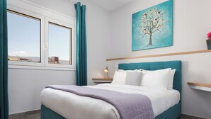 A bedroom with a bed, a nightstand, a lamp, a painting of a tree, and a window with curtains. - Acropolis Sandra Deluxe Apartment, Bill & John Apartments & Villas (Athens)