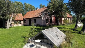 A rustic house with a red-tiled roof, surrounded by a well-maintained lawn and trees.