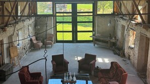 A spacious room with a high ceiling and large windows, furnished with several chairs and a table.
