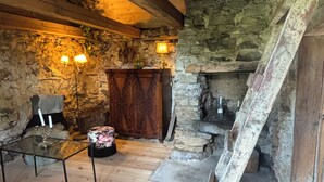 A rustic interior with stone walls, wooden beams, a fireplace, and a wooden staircase.