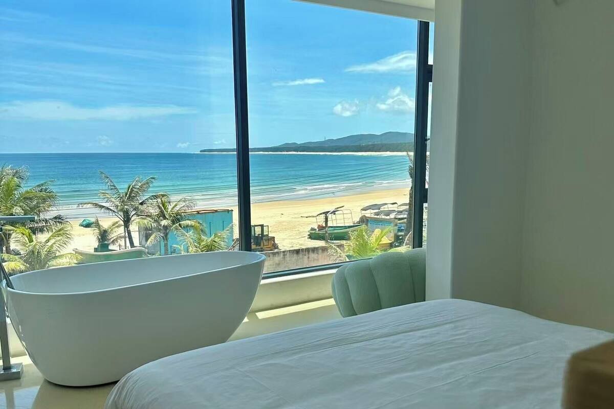 Un dormitorio con un ventanal grande con vistas a una playa y al océano.