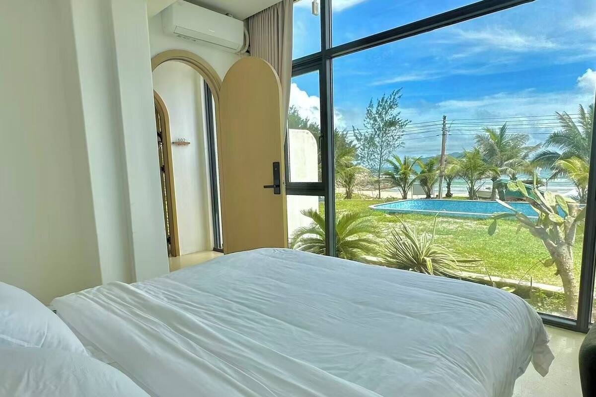 Habitación de hotel con una cama grande, una puerta y vistas a una piscina y palmeras.