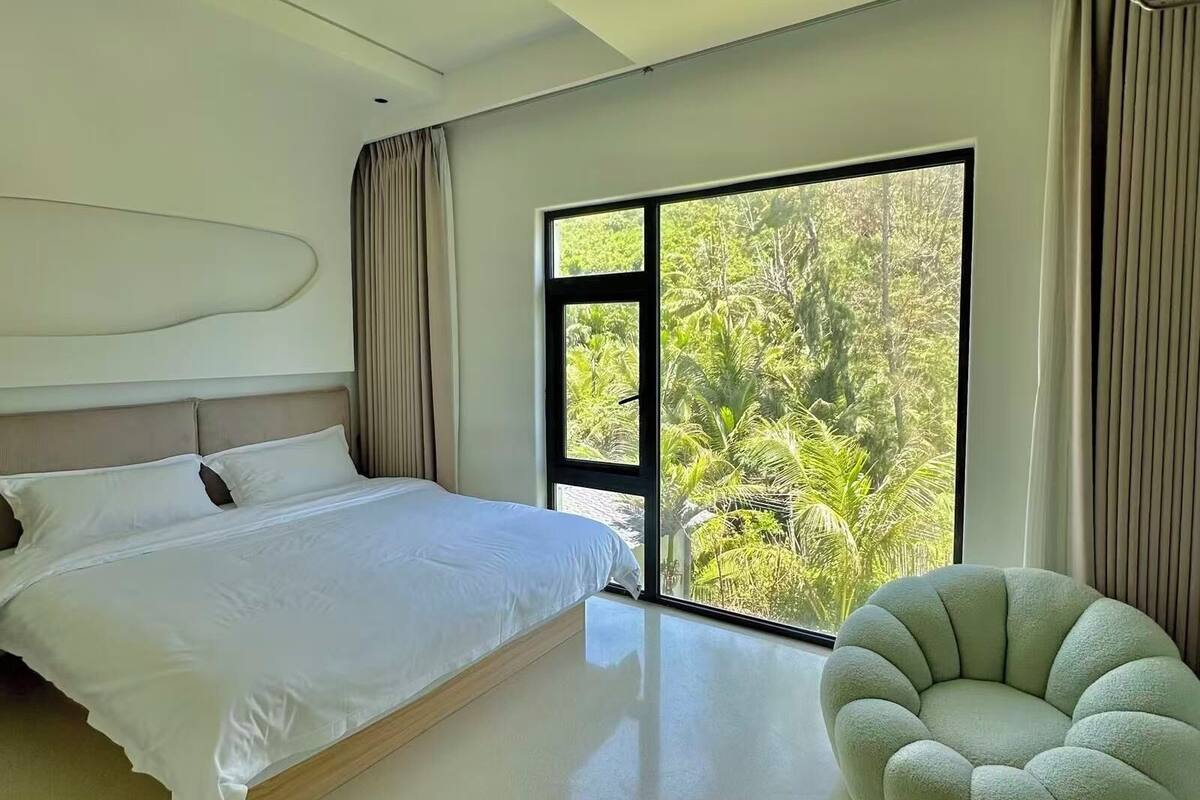 Un dormitorio moderno con una cama grande, vistas a zonas verdes a través de una puerta corredera y una silla verde llamativa.