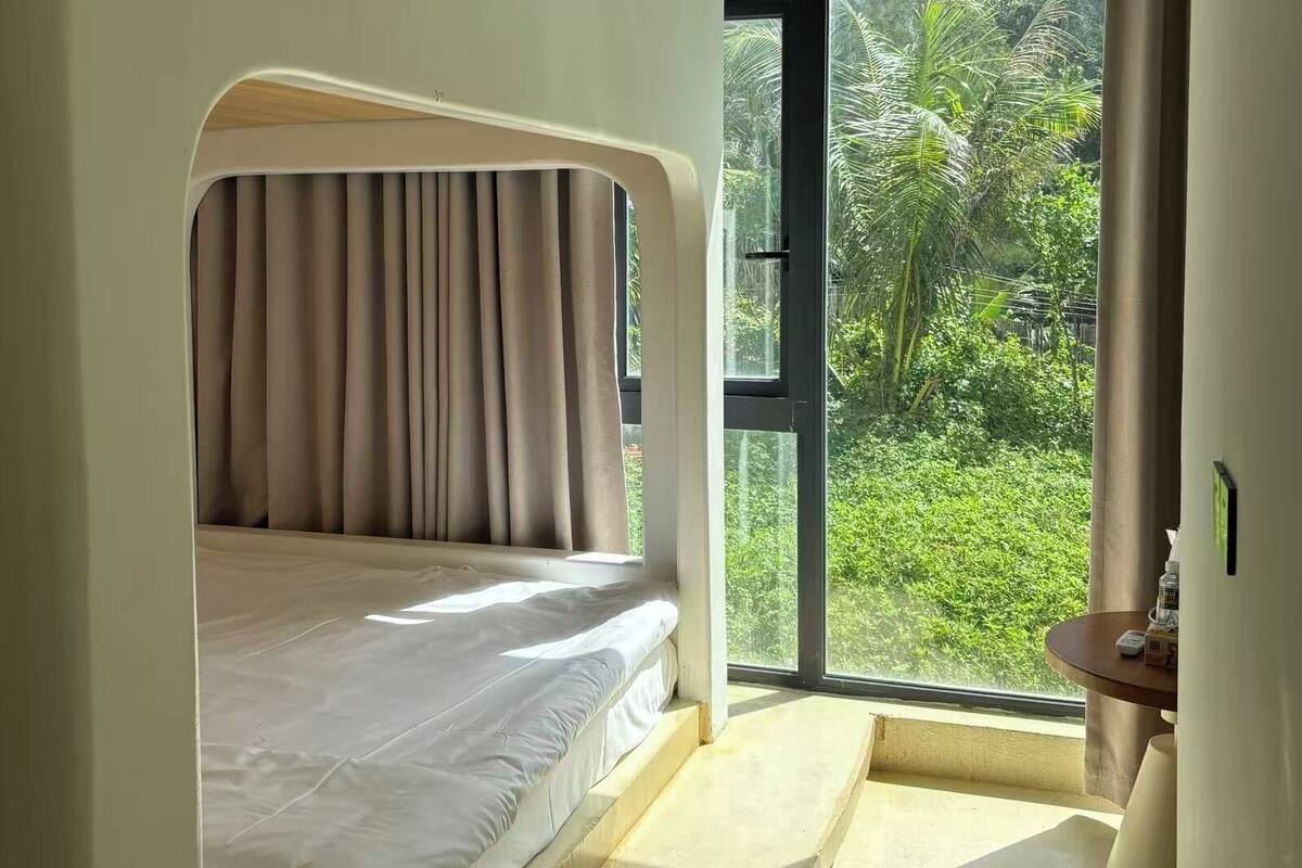 Un dormitorio con cama, ventana y vistas a la vegetación exterior.
