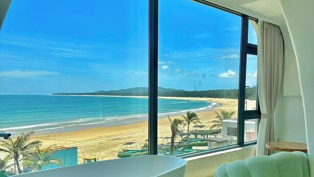 A modern bathroom with a large bathtub and a view of a beach and ocean. - Nirvana Seaview Homestay (Wanning)