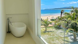 A modern bathroom with a freestanding bathtub and a balcony overlooking a beach with palm trees. - Nirvana Seaview Homestay (Wanning)