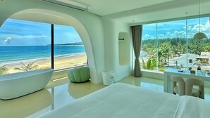 A modern hotel room with a large bed, a curved seating area, and a view of the beach and palm trees. - Nirvana Seaview Homestay (Wanning)