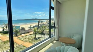 A room with a large window overlooking a beach, a small round table, and a unique tufted chair. - Nirvana Seaview Homestay (Wanning)