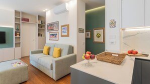 Ein modernes Wohnzimmer mit einem grauen Sofa, einem kleinen Tisch mit Früchten und einer Küchenzeile mit Marmorarbeitsplatte.