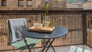 Ein Balkon mit rundem Tisch, einem Stuhl, einer Vase mit Blumen und einem Tablett mit Schüssel und Gläsern.