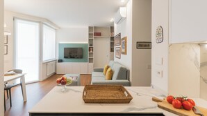 Eine moderne Küche mit Kochinsel, ein Essbereich mit Tisch und Stühlen, ein Wohnzimmer mit Sofa und Fernseher sowie ein Badezimmer mit Dusche und Toilette.