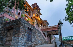A traditional stone building with multiple balconies, potted plants, and a bridge. - Shrisiddhpuram (Kumbhalgarh)