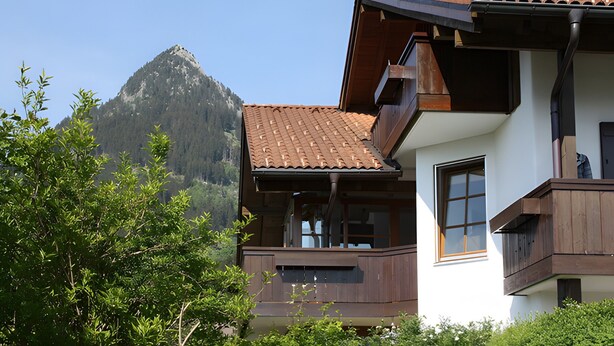 Un chalet de montagne doté d’un balcon, de grandes fenêtres et offrant une vue sur la montagne.