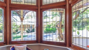 A corner room with large windows, two chairs, a small table, and a red carpet.