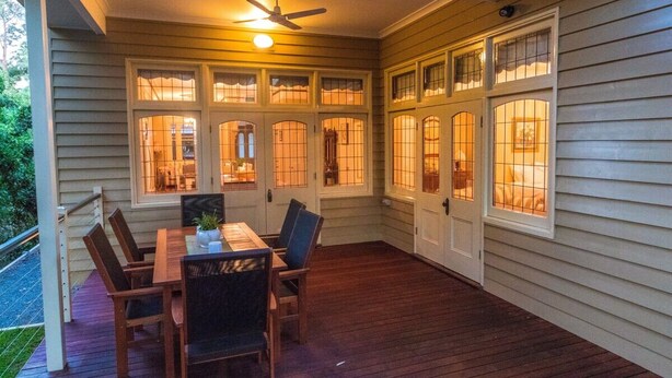 A covered patio with a wooden table and chairs, large windows with glass panes, and a ceiling fan.