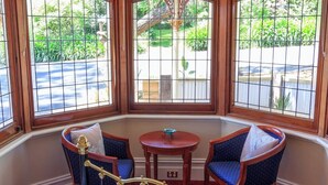 A hotel room with a large bed, two blue upholstered chairs, a small round table, and a view of a garden through large windows.