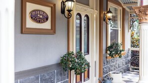 A framed sign reading "Rosebery Cottage" above a door, with two potted plants and a watering can on the porch.