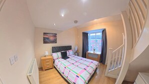 A bedroom with a bed, bedside table, lamp, and a window with curtains. - Northampton Oasis Retreat - 3-4 Bedroom House (Northampton)
