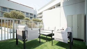 Ein Balkon mit künstlichem Gras, weißer Möbel und Blick auf ein modernes Gebäude.