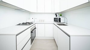 Eine moderne Küche mit weißen Schränken, einem Gasherd, einem Backofen, einer Mikrowelle und einem Spülbecken.