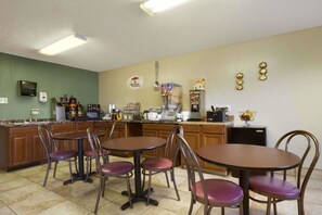 Un espace dédié au petit-déjeuner, équipé d’une machine à café, d’un four à micro-ondes et d’un réfrigérateur. Il y a quatre chaises et une table.
