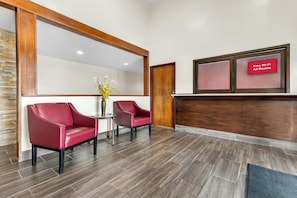 A reception area with a wooden reception desk, two red leather chairs, a small table with a vase of flowers, and a sign indicating free Wi-Fi in all rooms. - Red Roof Inn Huntsville, AL (Huntsville)