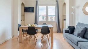 A modern living room with a grey sofa, a dining table with chairs, and a large window with curtains. - Stunning views over iconic Sagrada Familia! Building perfect for large groups! (Barcelona)