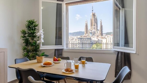 A dining area with a table set for breakfast, a potted plant, and a view of a historic building. - Stunning views over iconic Sagrada Familia! Building perfect for large groups! (Barcelona)
