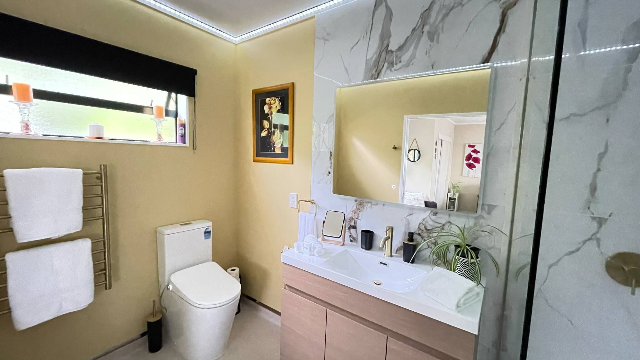 A bathroom with a toilet, sink, mirror, and towel rack.