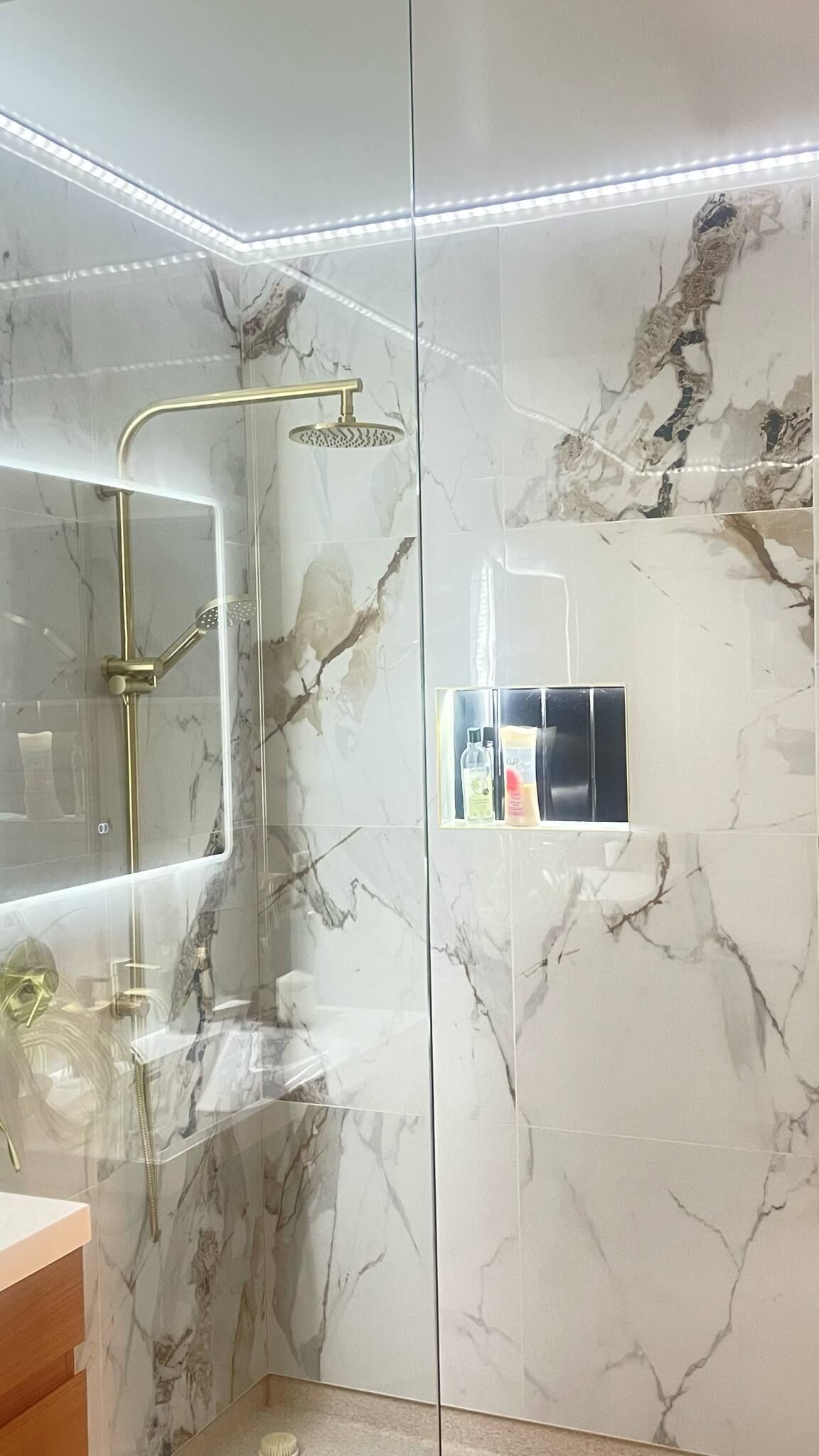 Un baño moderno con ducha de vidrio, paredes de mármol y tocador empotrado con espejo.