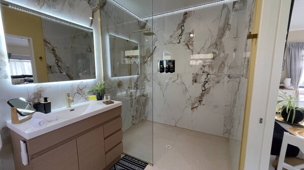 Une salle de bain moderne avec un mur en marbre, un grand miroir, un meuble-lavabo et un espace douche.