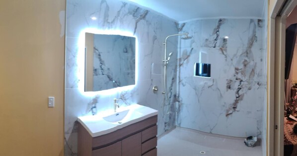 Un baño moderno con pared de mármol, tocador con espejo y zona de ducha.