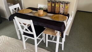 Een eettafel met een zwarte tafelkleed, witte stoelen en een kleine potplant.