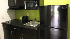 A compact kitchen with dark cabinets, a black microwave, a black refrigerator, a sink, and a toaster.