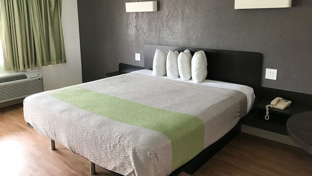 A modern hotel room with a large bed, a bedside table with a phone, and a window with curtains.
