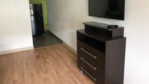 A room with a flat-screen TV mounted on the wall, a dark wooden entertainment unit with drawers, and a wooden floor.