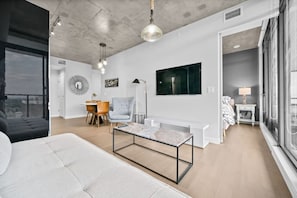 Uma sala de estar moderna com sofá, mesa de centro, área de jantar com cadeiras, televisão e uma janela grande.