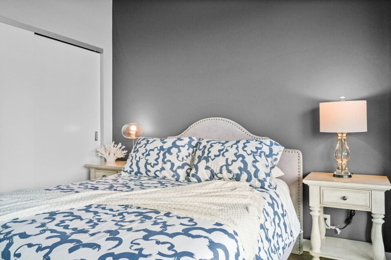 A bedroom with a bed, a bedside table with a lamp, and a nightstand with a decorative item.