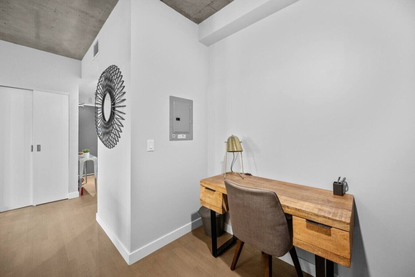 A modern office space with a wooden desk, a grey office chair, a wall-mounted light, and a decorative mirror.