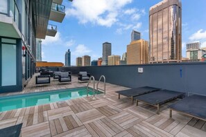 Área de piscina no terraço com espreguiçadeiras e vista para o horizonte da cidade.