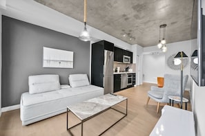 Uma sala de estar moderna com um sofá, uma mesa de centro e uma cozinha ao fundo.