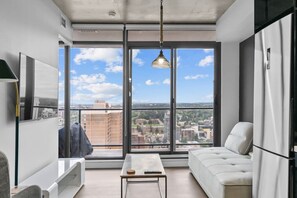 Un appartement moderne doté d’une grande fenêtre, d’un canapé, d’une table basse et d’un réfrigérateur.
