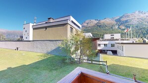 A modern building with a flat roof and a stone wall, surrounded by a grassy area and mountains in the background. - Centrally located residential complex in St. (St. Moritz)
