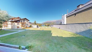 A residential area with a grassy courtyard, a building with balconies, and a stone wall. - Centrally located residential complex in St. (St. Moritz)