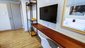 A hotel room with a wooden desk, a TV mounted on the wall, a bed with white bedding, and a painting of a snowy forest.