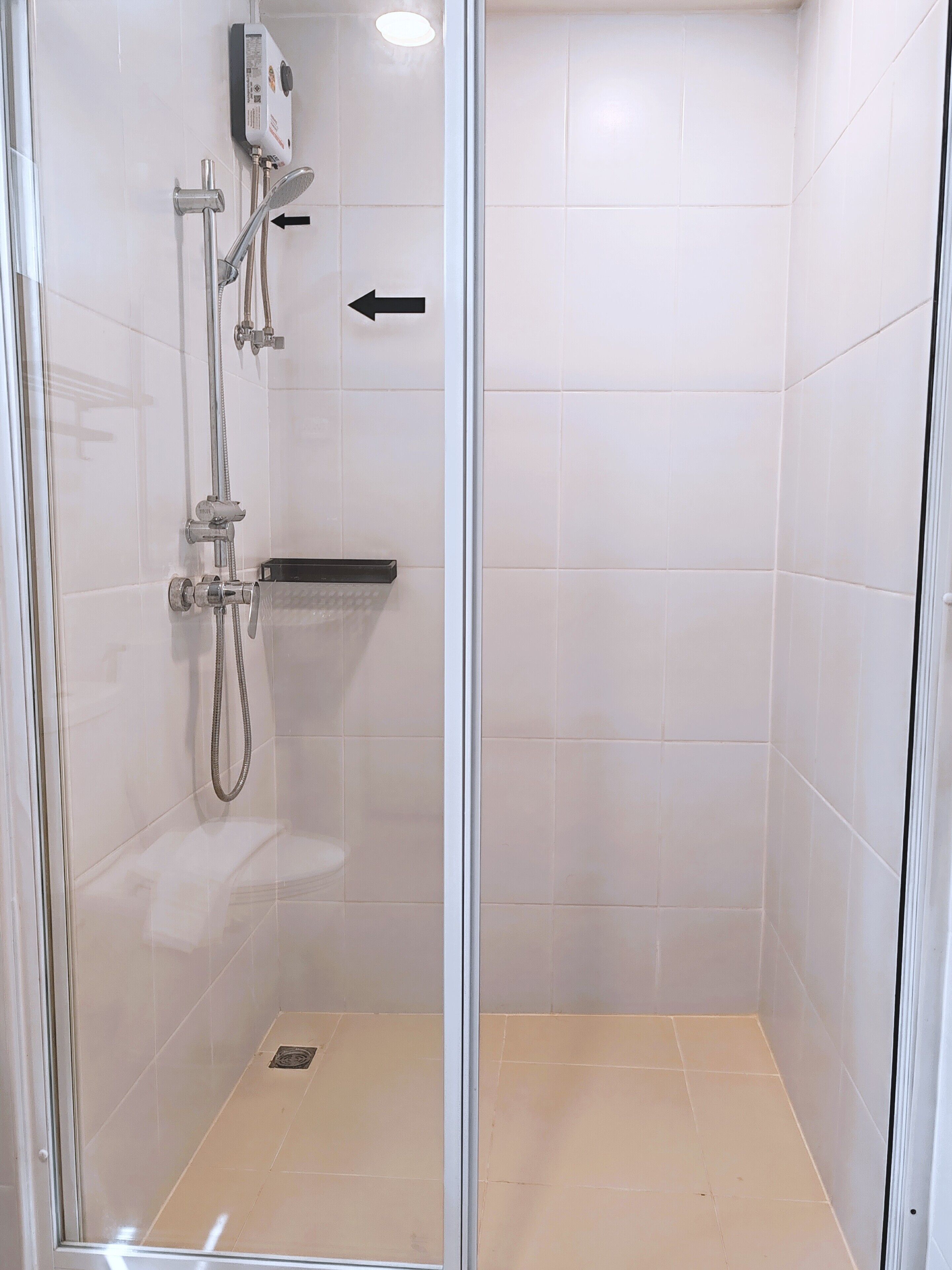 Une cabine de douche fermée par des parois en verre, dotée d’un pommeau de douche à main, d’un robinet mural et d’un panneau de commande.