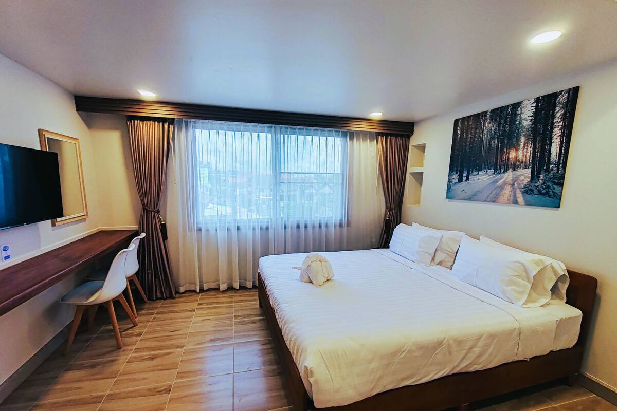 Ein Hotelzimmer mit Bett, Schreibtisch, Stuhl, Fernseher und einem Bild an der Wand.