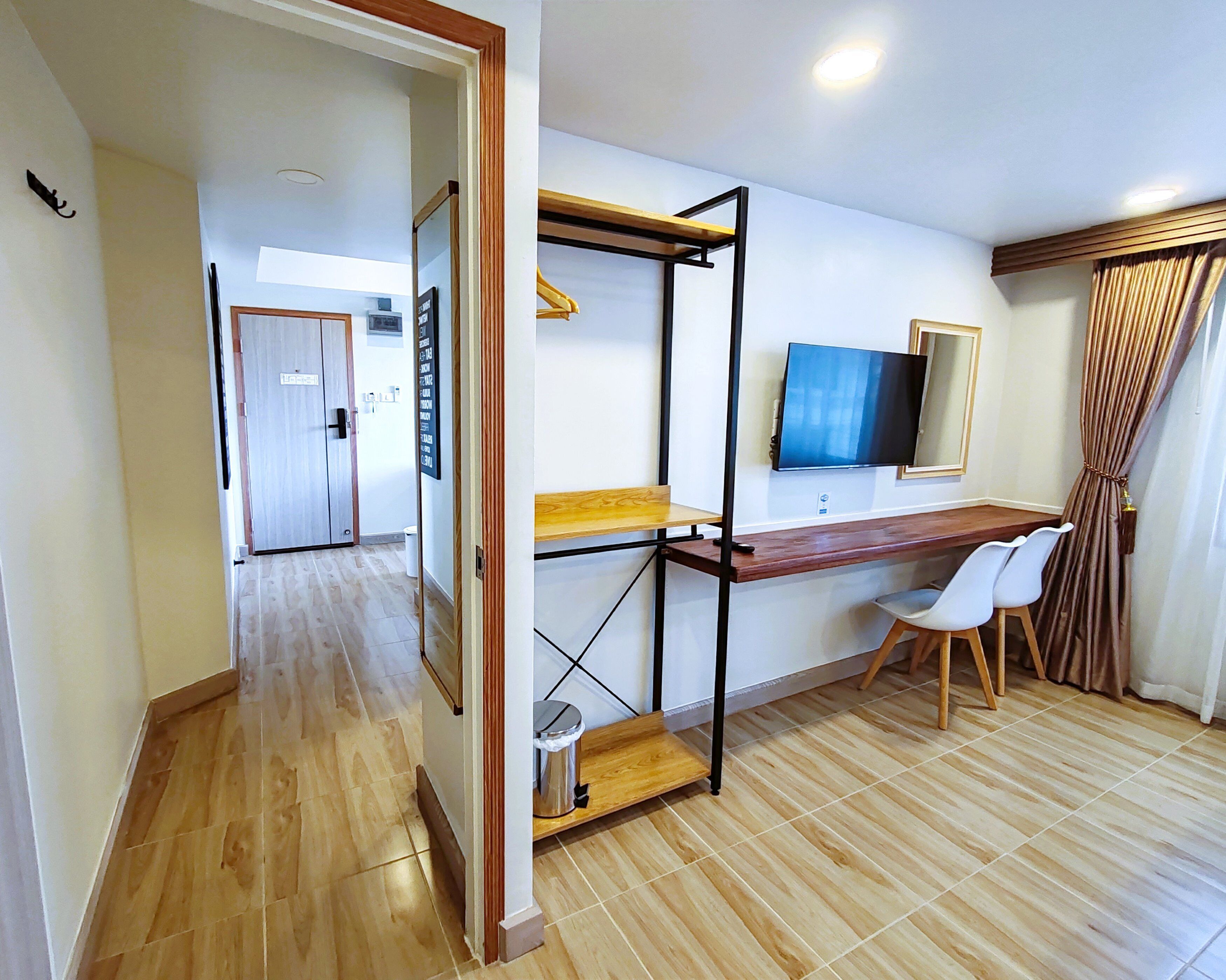 A compact room with a desk, a chair, a television, and a window with curtains.